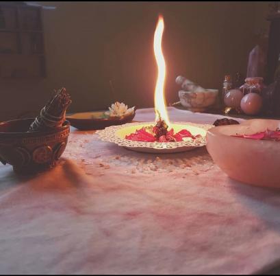 Lighted candle with various herbs, bowls and sage on table